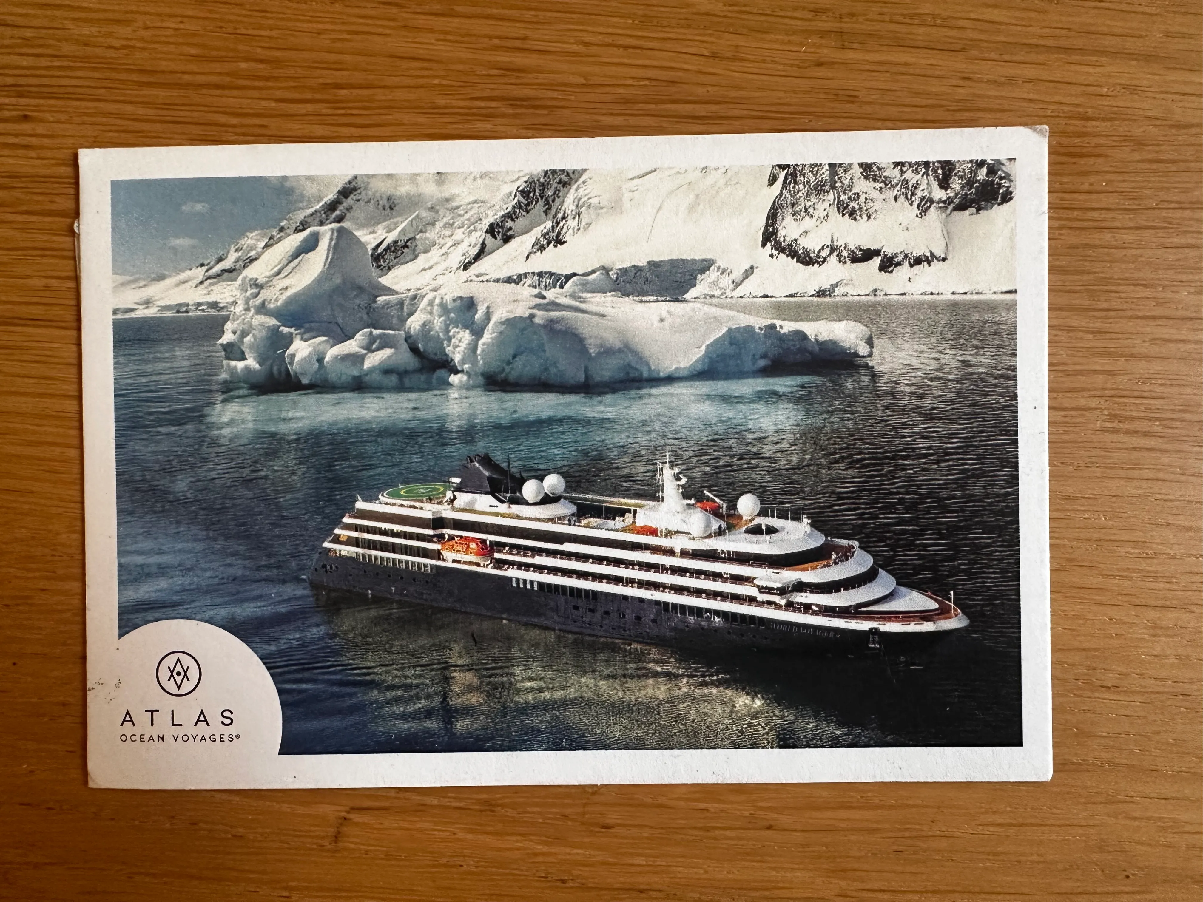 A postcard with an image on it, taken in Antarctica. In the foreground is a cruise ship, and in the background is some ice and further back some icy mountains.