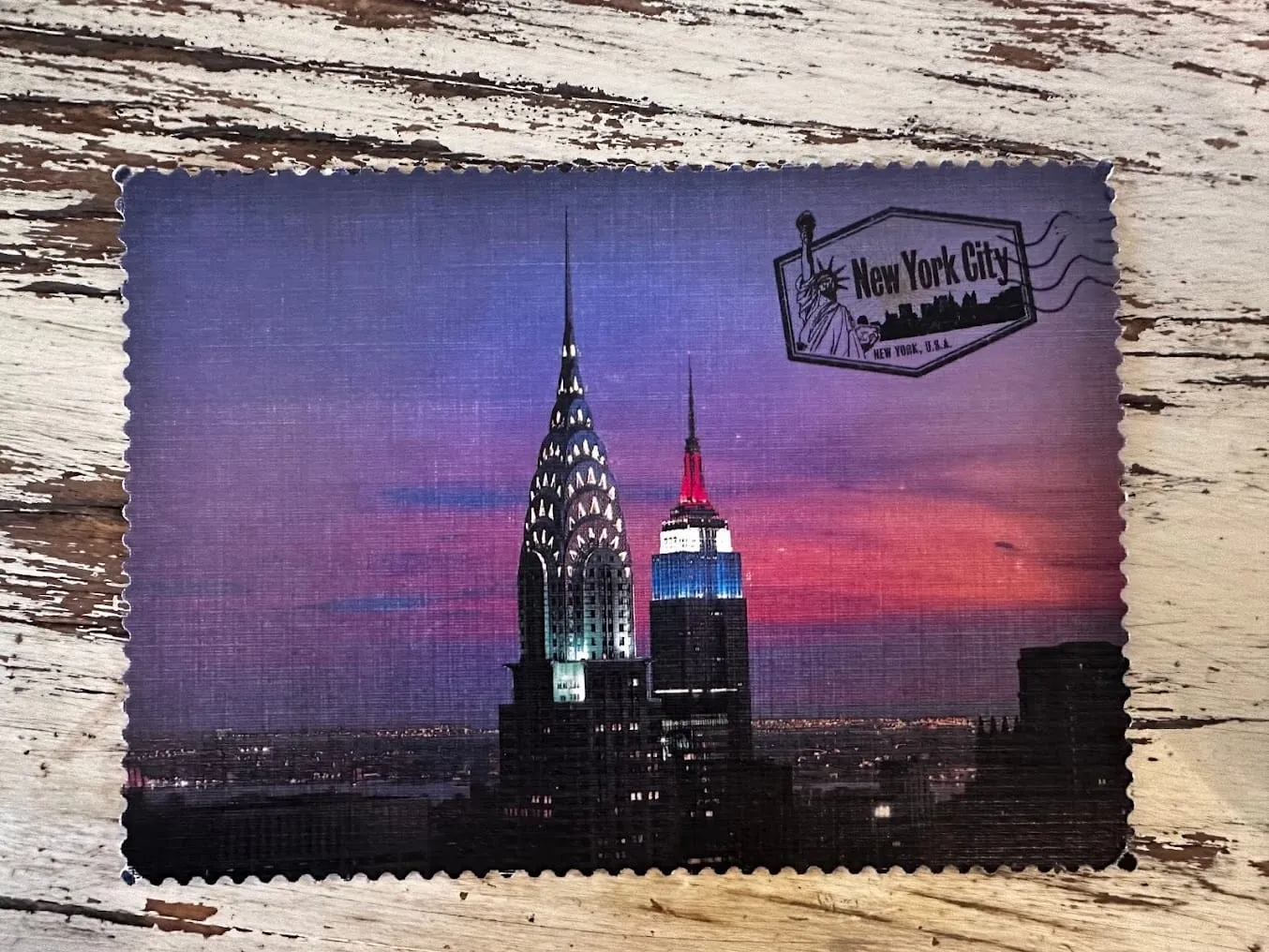 A photo of a postcard, with an abstract version of the NYC skyline, the Empire State Building is in focus and it is just after sunset with a pink sky